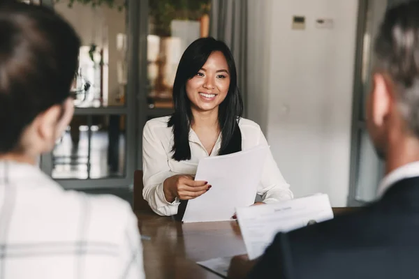 Young woman smiling and holding resume while interviewing as candidate for job in big company